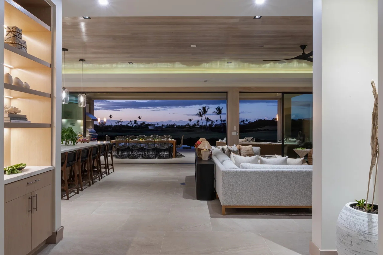 An open-plan living and dining area with seating facing large windows at dusk.