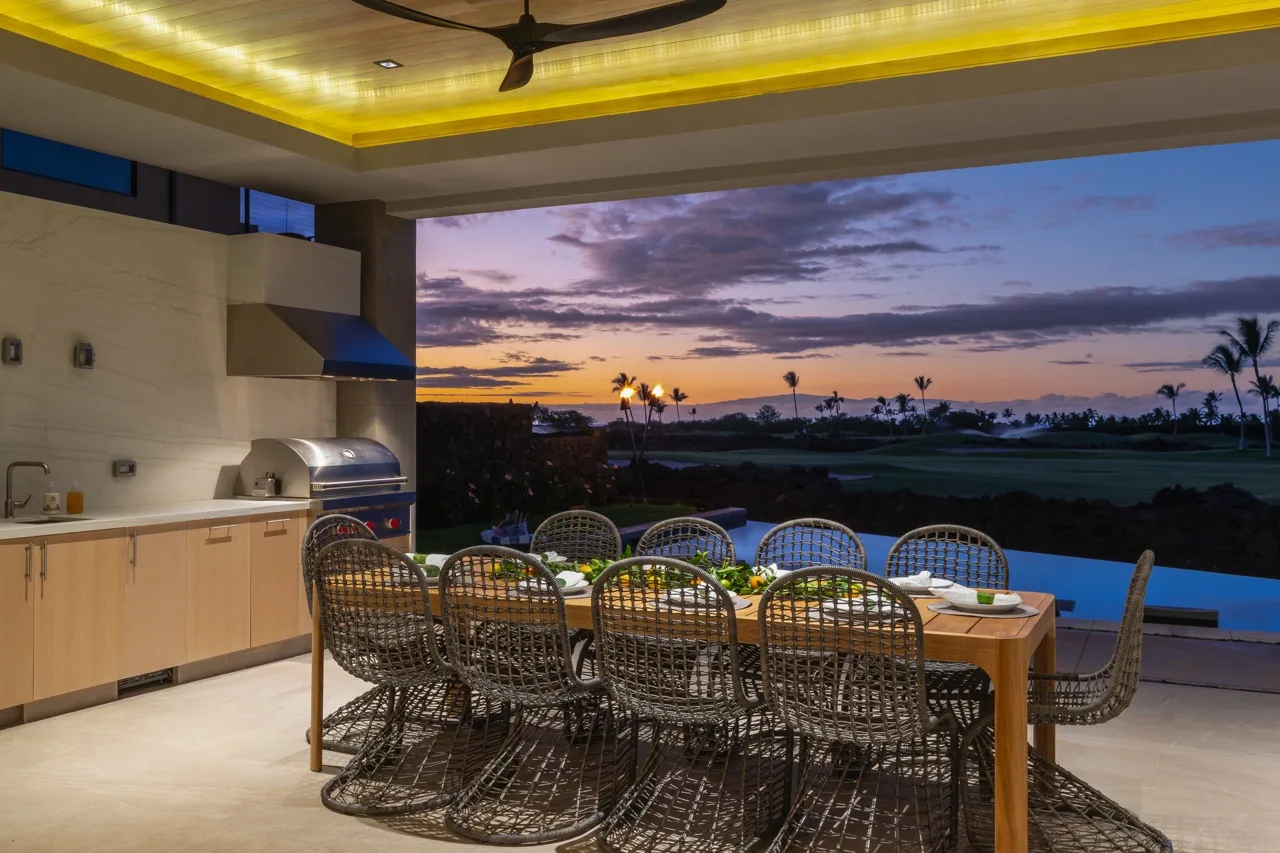 An outdoor dining area with a long table overlooks a sunset landscape.