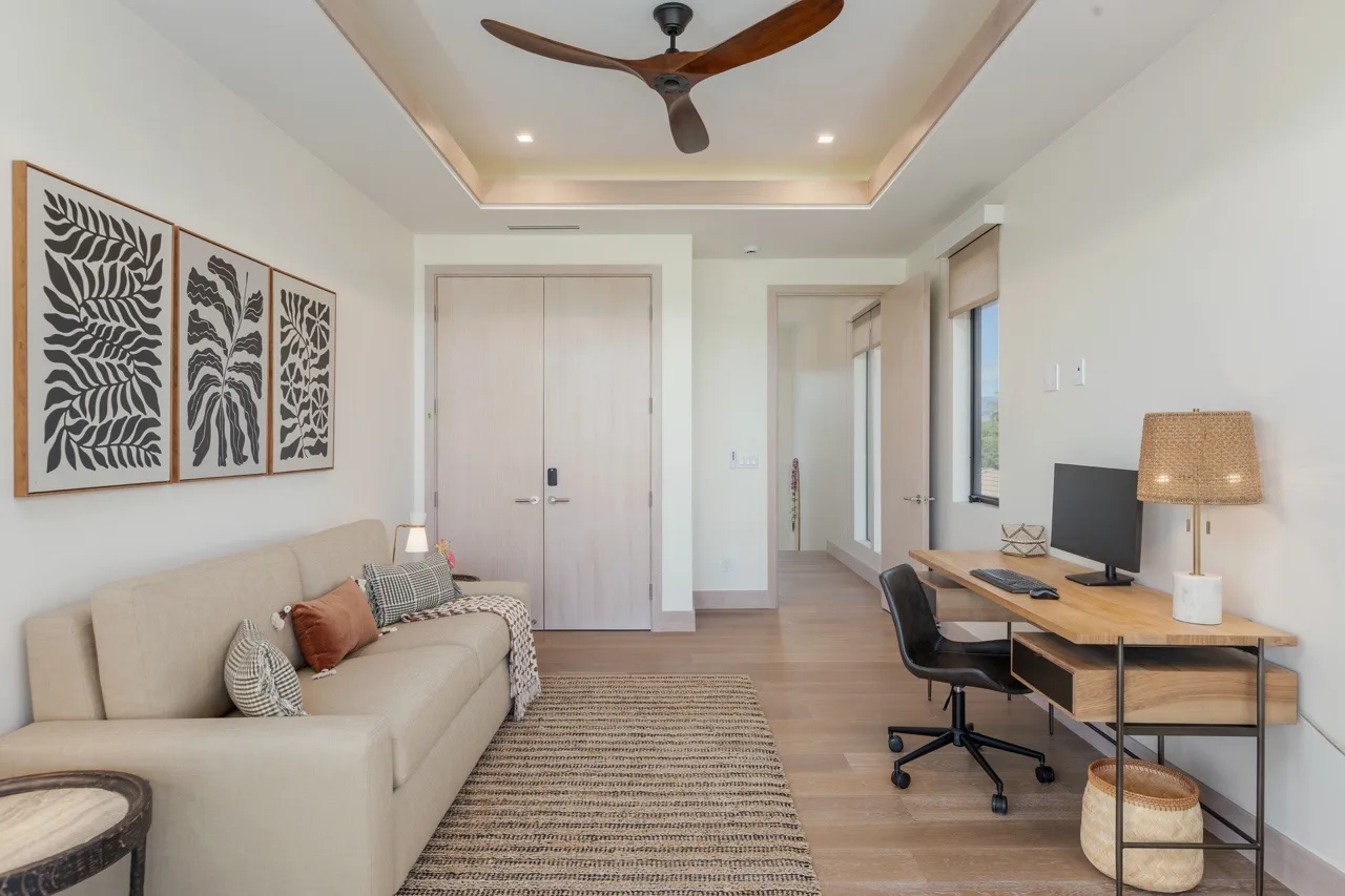 A bright living and work area with a sofa, desk, and ceiling fan.