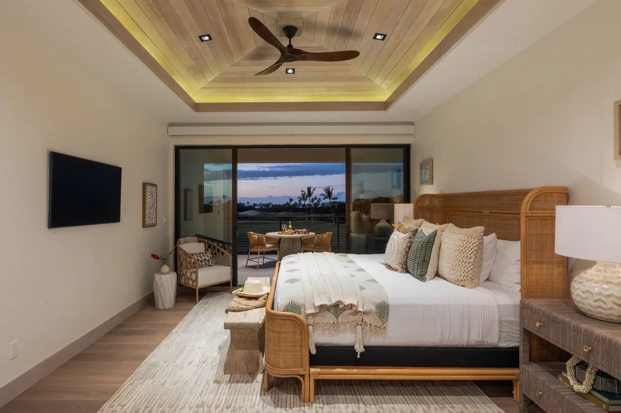 A bedroom with a large bed facing sliding glass doors and a coastal view.