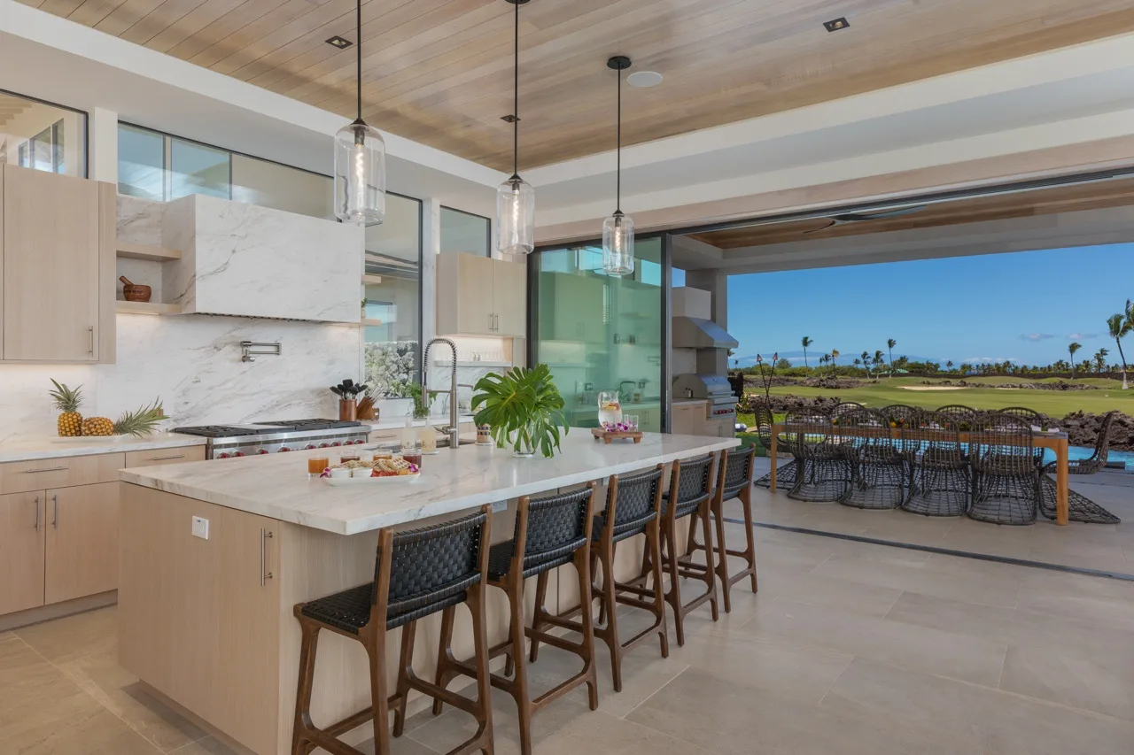An open kitchen with a long island and seating faces a patio and golf course.