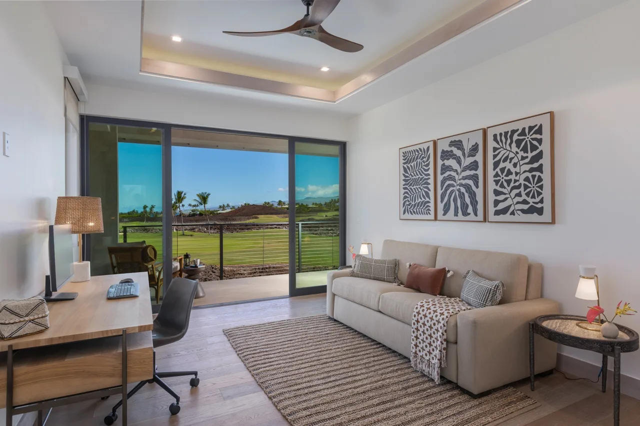 A bright living room with seating, a desk, and wide windows overlooking greenery.