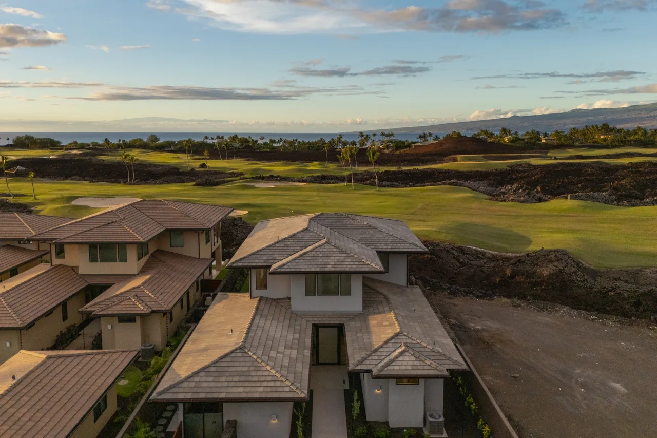 Aerial view of houses beside a green golf course, with the ocean in the distance.