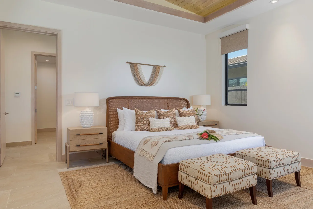 A bedroom with a bed, patterned cushions, and two upholstered footstools.