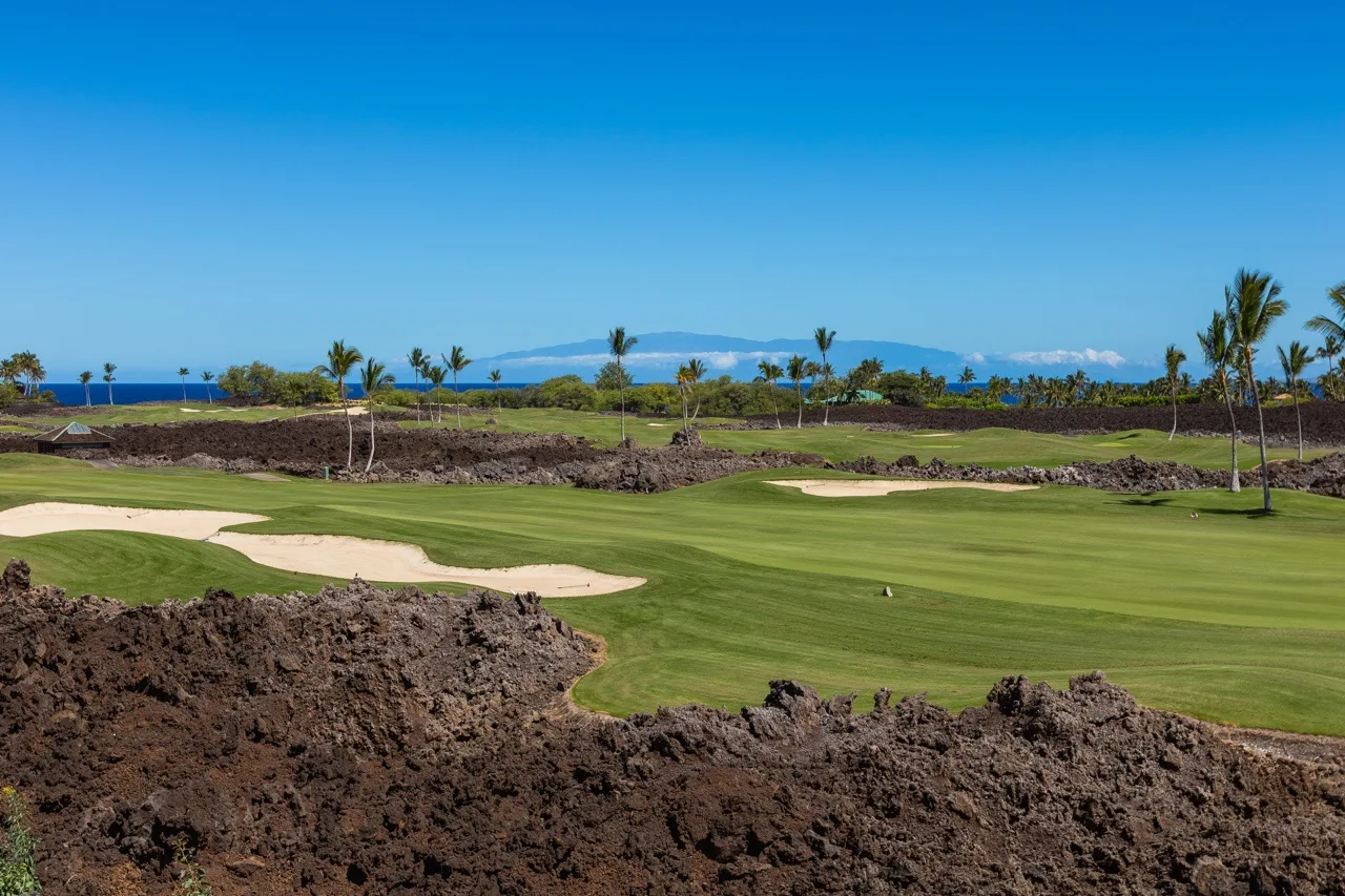 A golf course with green fairways and sand bunkers sits beside a rocky landscape.