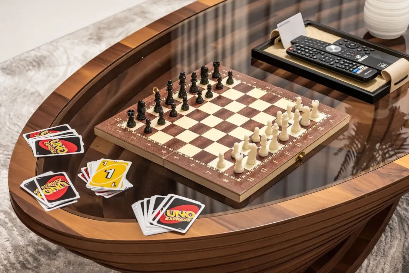 A game table displays a chessboard, playing cards, and a television remote.