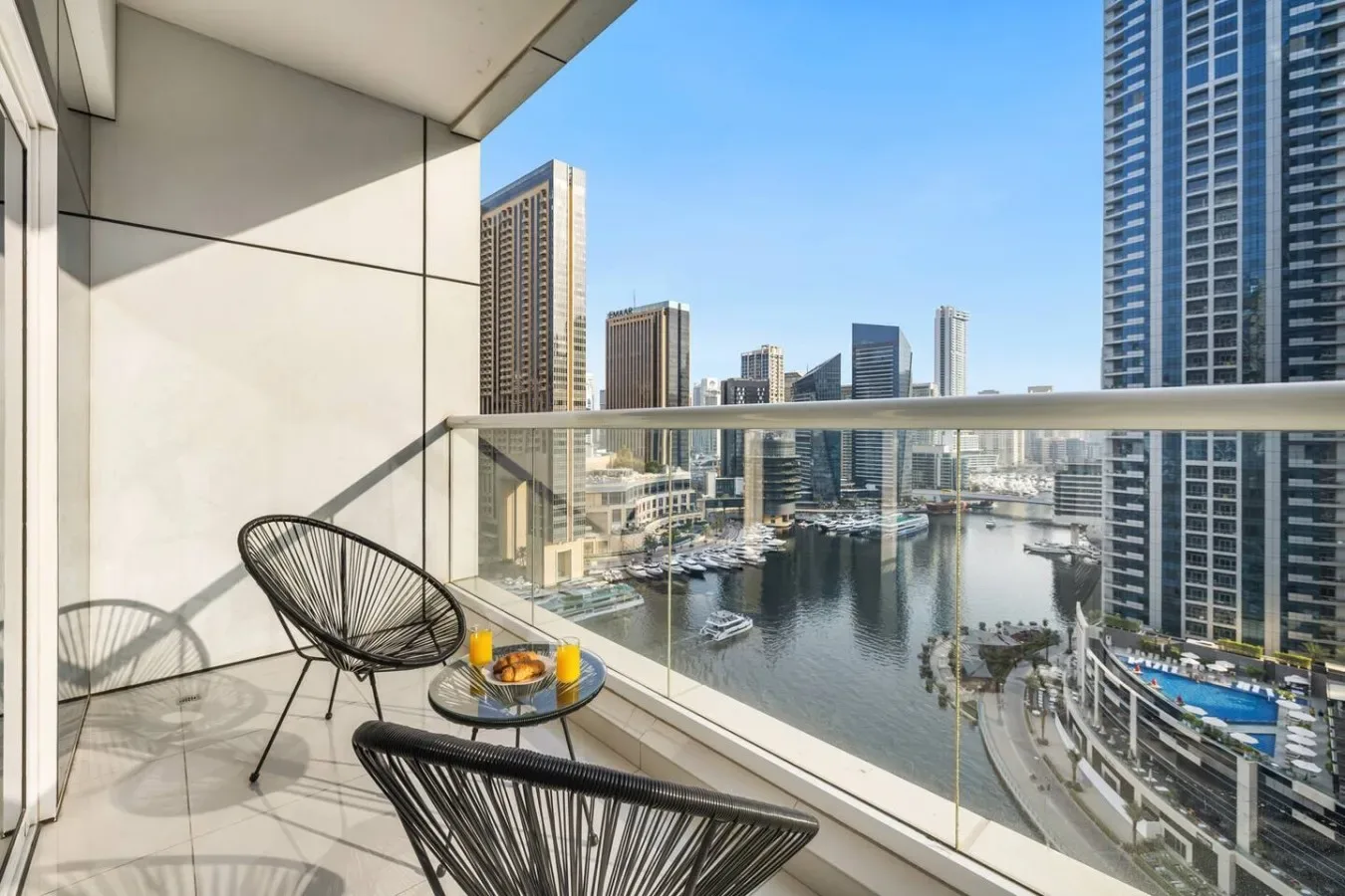A balcony with outdoor seating overlooks a waterfront lined with high-rise buildings.