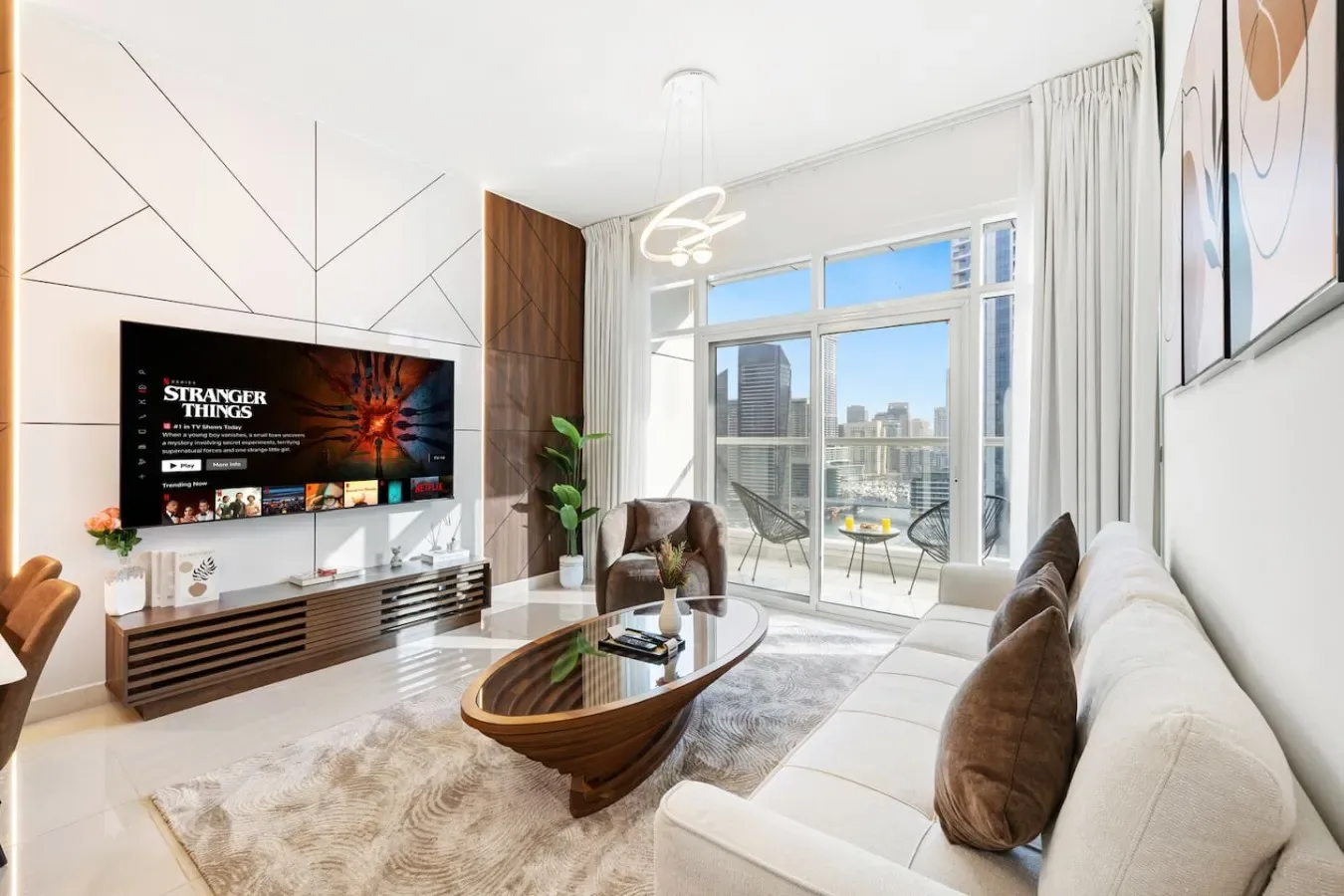 A bright living room with a large window, seating, and a television.