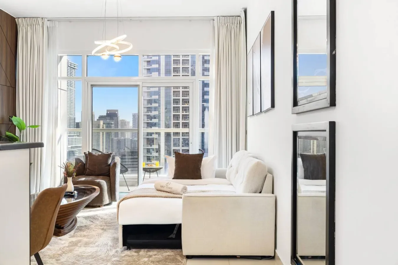 A bright living room with white seating and large windows overlooking nearby buildings.