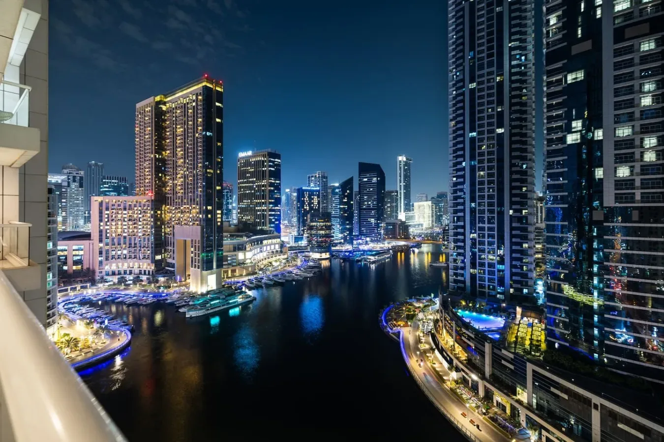 A nighttime city skyline reflects across a waterway between illuminated high-rise buildings.