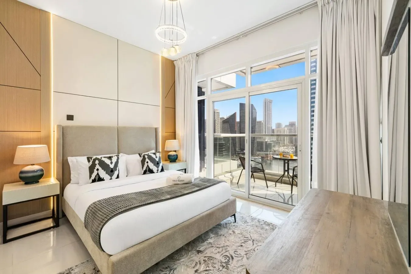 A modern bedroom with a bed beside large windows overlooking city buildings.