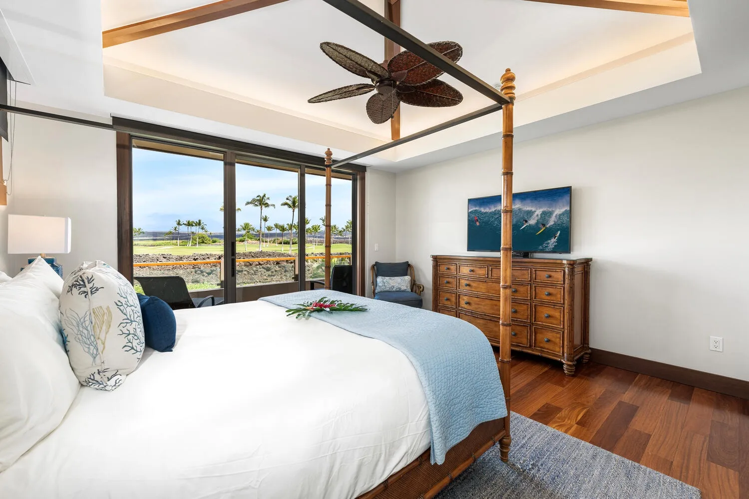 Dormitorio con cama, cómoda de madera y ventanas con vistas a palmeras.