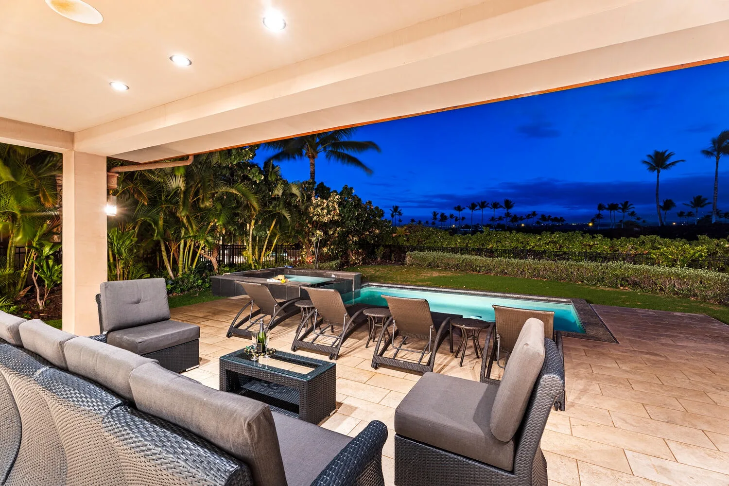 Un patio exterior cubierto con asientos da a una piscina y un jardín tropical.