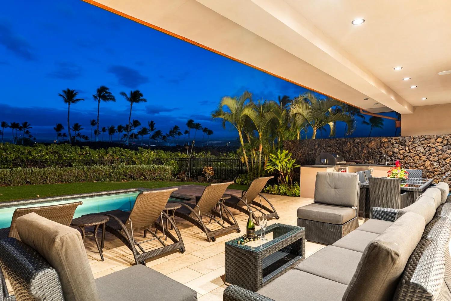 Un patio exterior con asientos junto a una piscina, con palmeras al atardecer.