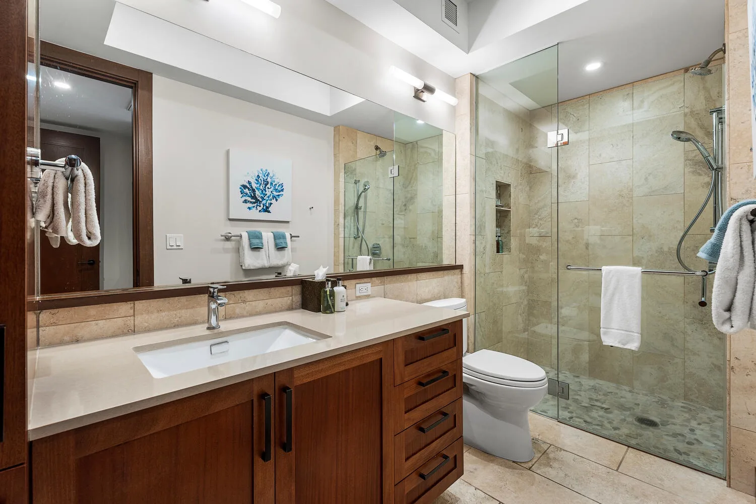 Un baño con un tocador largo, lavabo y ducha de vidrio.