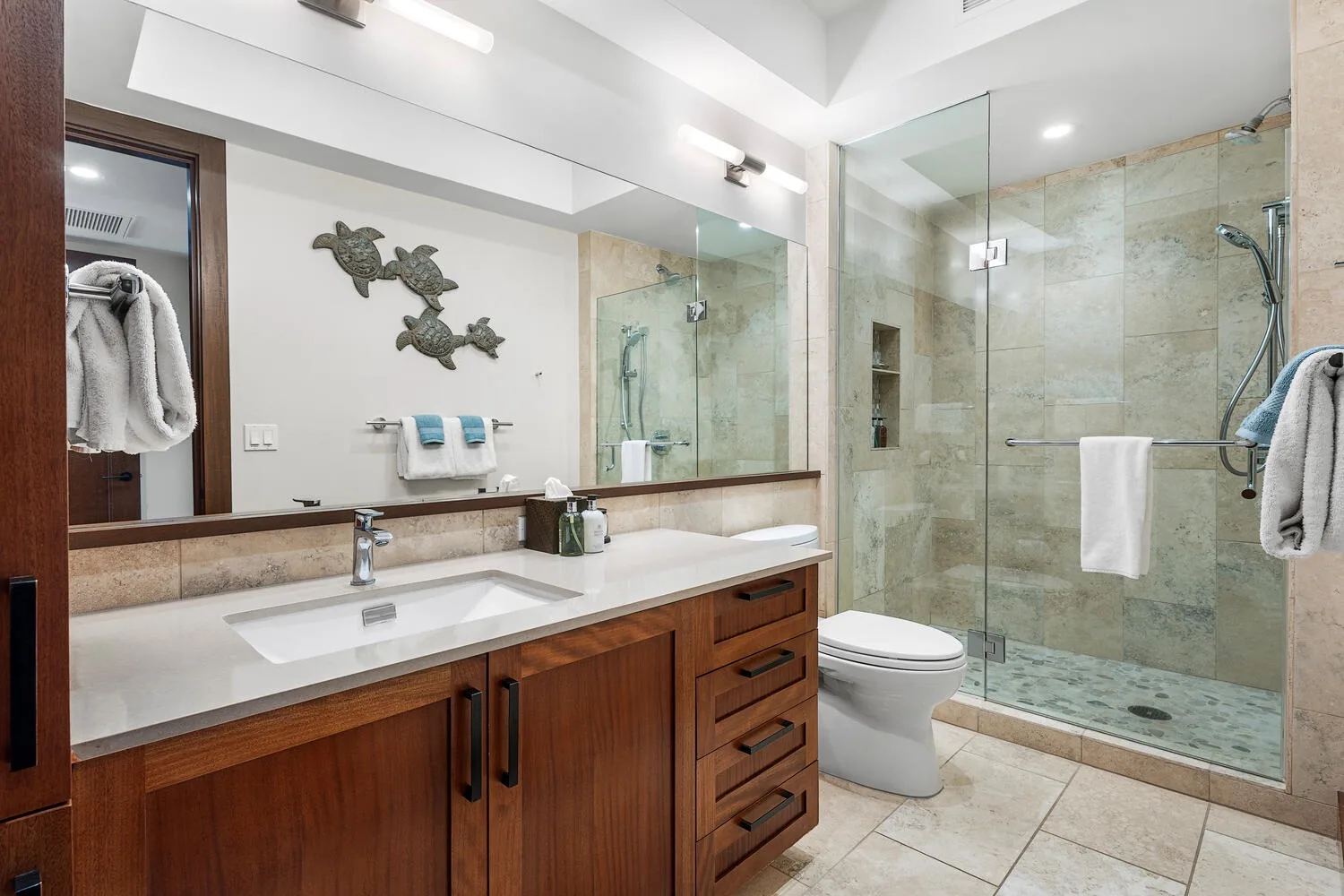 Un baño luminoso con un tocador largo, lavabo y ducha con mampara de vidrio.