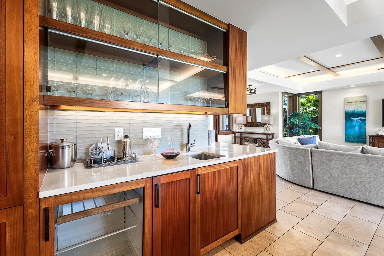 Una cocina abierta al salón, con gabinetes de madera y una zona de asientos gris.
