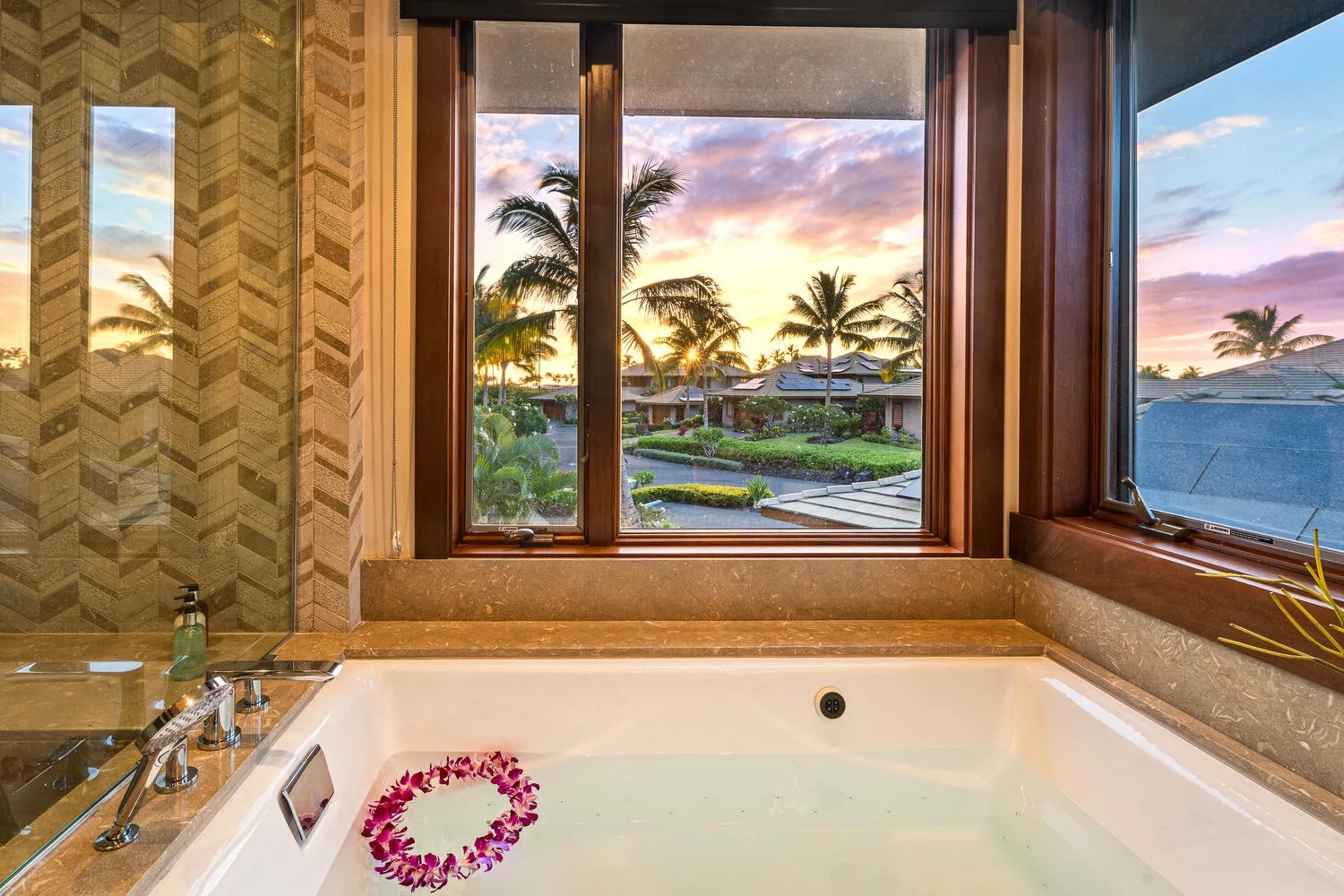 Una bañera está bajo grandes ventanas con vistas a palmeras y al atardecer.