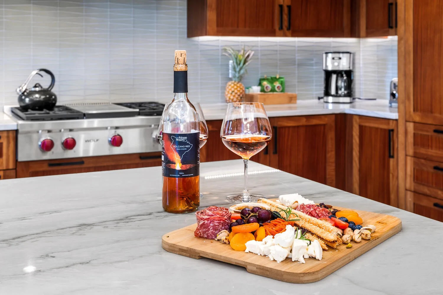 Una isla de cocina muestra una botella de vino, una copa y una tabla de charcutería.