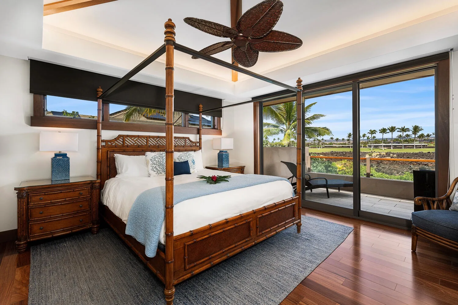 Un dormitorio con una cama con dosel de madera junto a grandes puertas de vidrio que dan a un balcón.