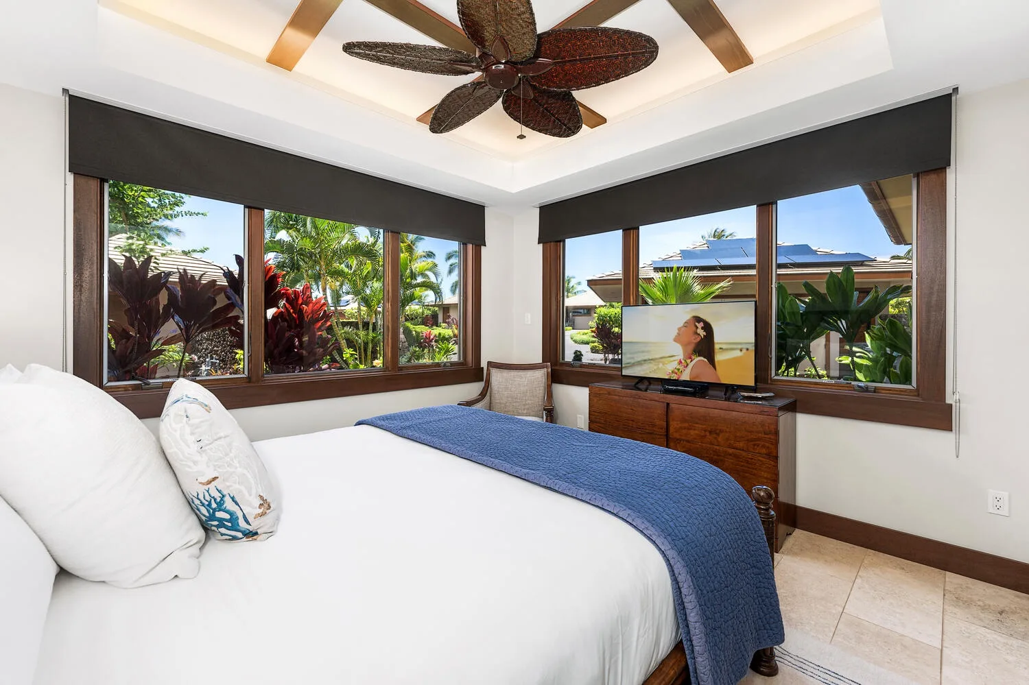 Un dormitorio luminoso con una cama blanca, una colcha azul y amplias ventanas con vistas a la vegetación.