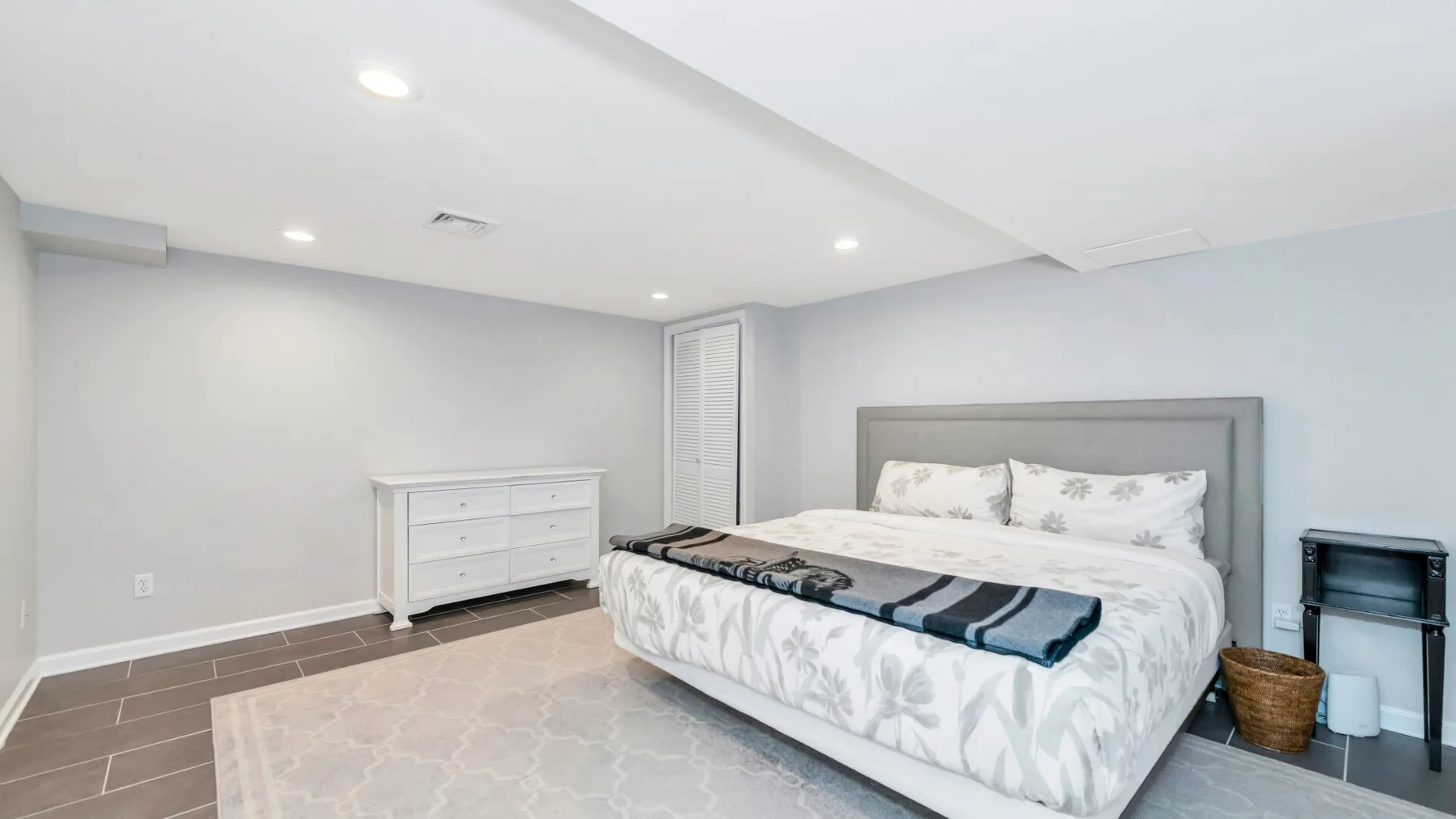 Un dormitorio con una cama y una cómoda blanca junto a una pared gris clara.
