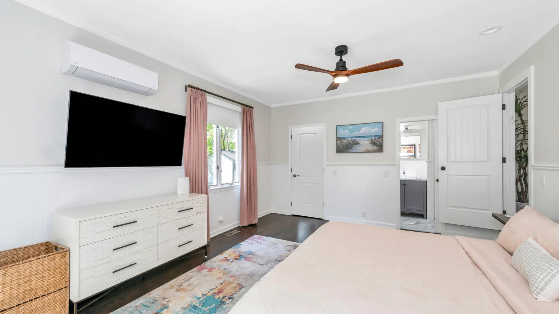 Un dormitorio luminoso con una cama, un televisor montado en la pared y un ventilador de techo.