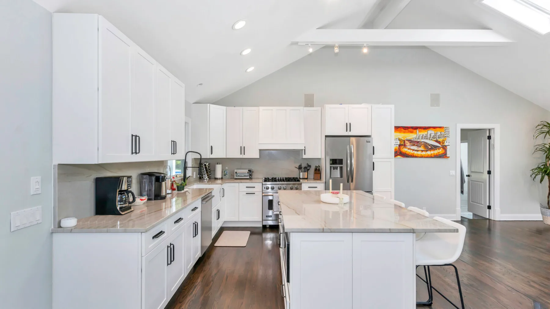 Una cocina luminosa con gabinetes blancos, electrodomésticos de acero inoxidable y una isla central.
