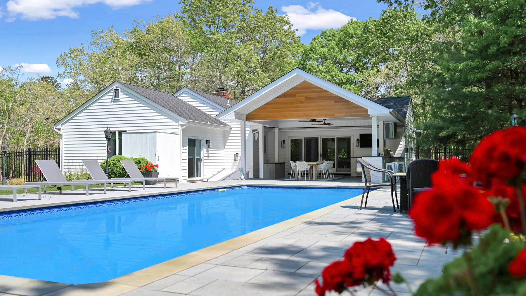Una piscina al aire libre junto a una casa con un patio cubierto.