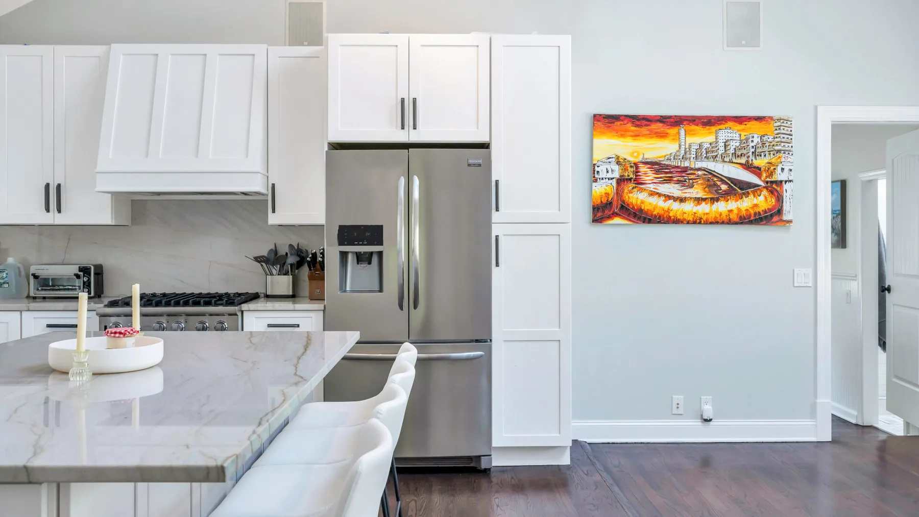 Una cocina luminosa con gabinetes blancos, electrodomésticos de acero inoxidable y una isla con patrón de mármol.