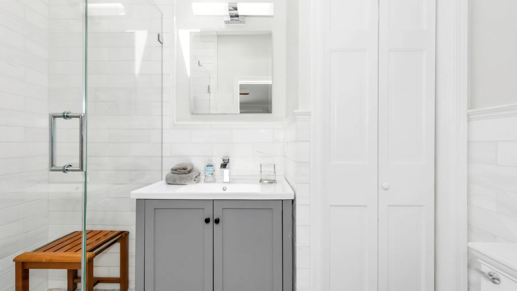 Un baño luminoso con un mueble gris y una ducha de vidrio.