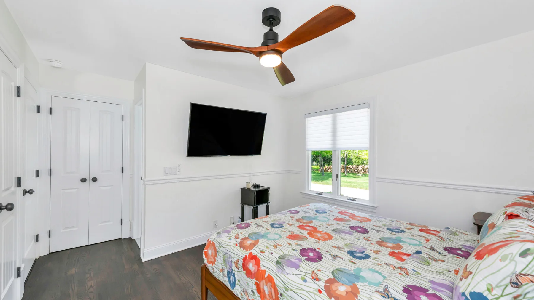 Un dormitorio luminoso con una colcha floral colorida y un televisor montado en la pared.