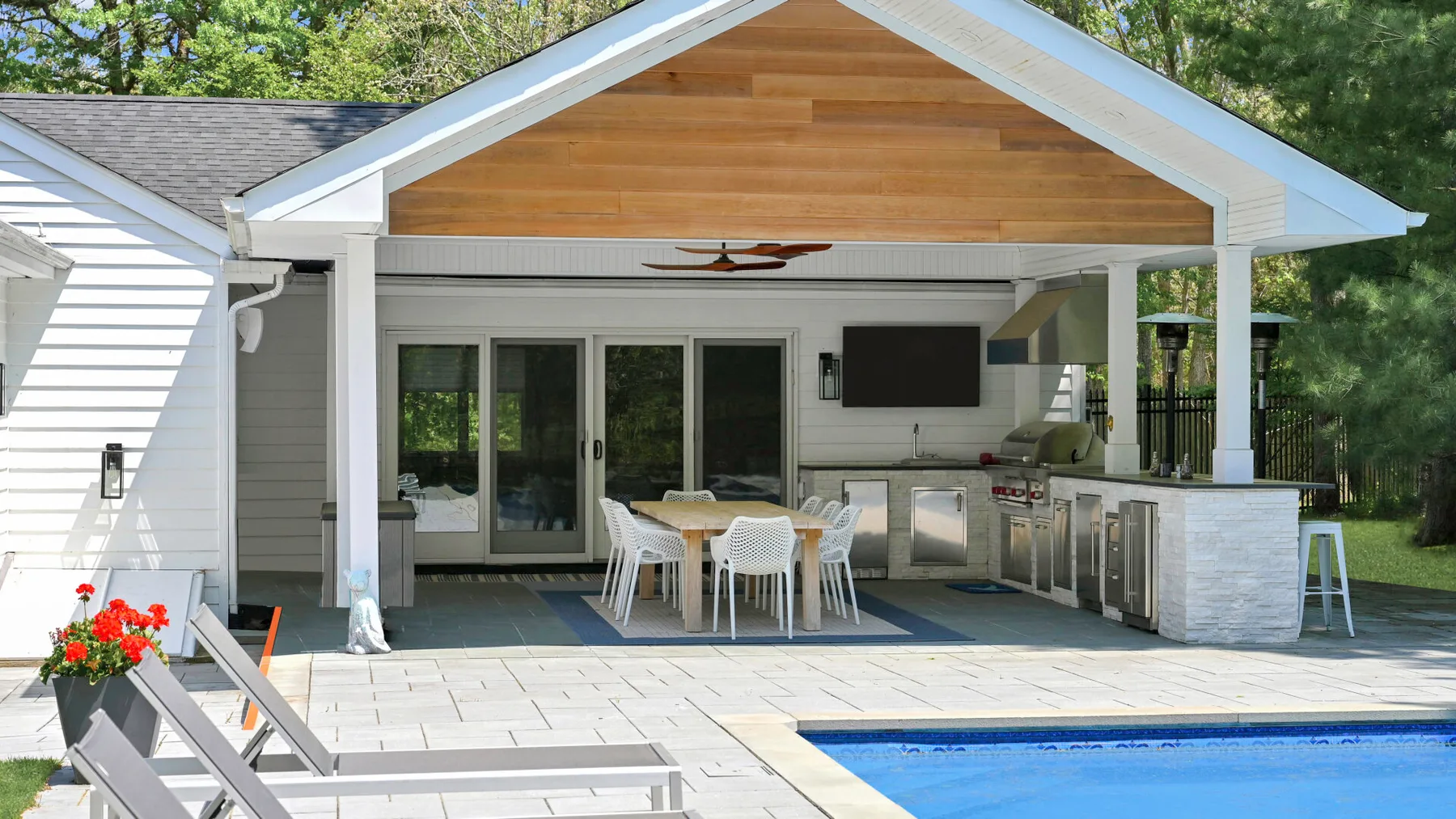 Una cocina y zona de comedor al aire libre y cubierta da a una piscina.