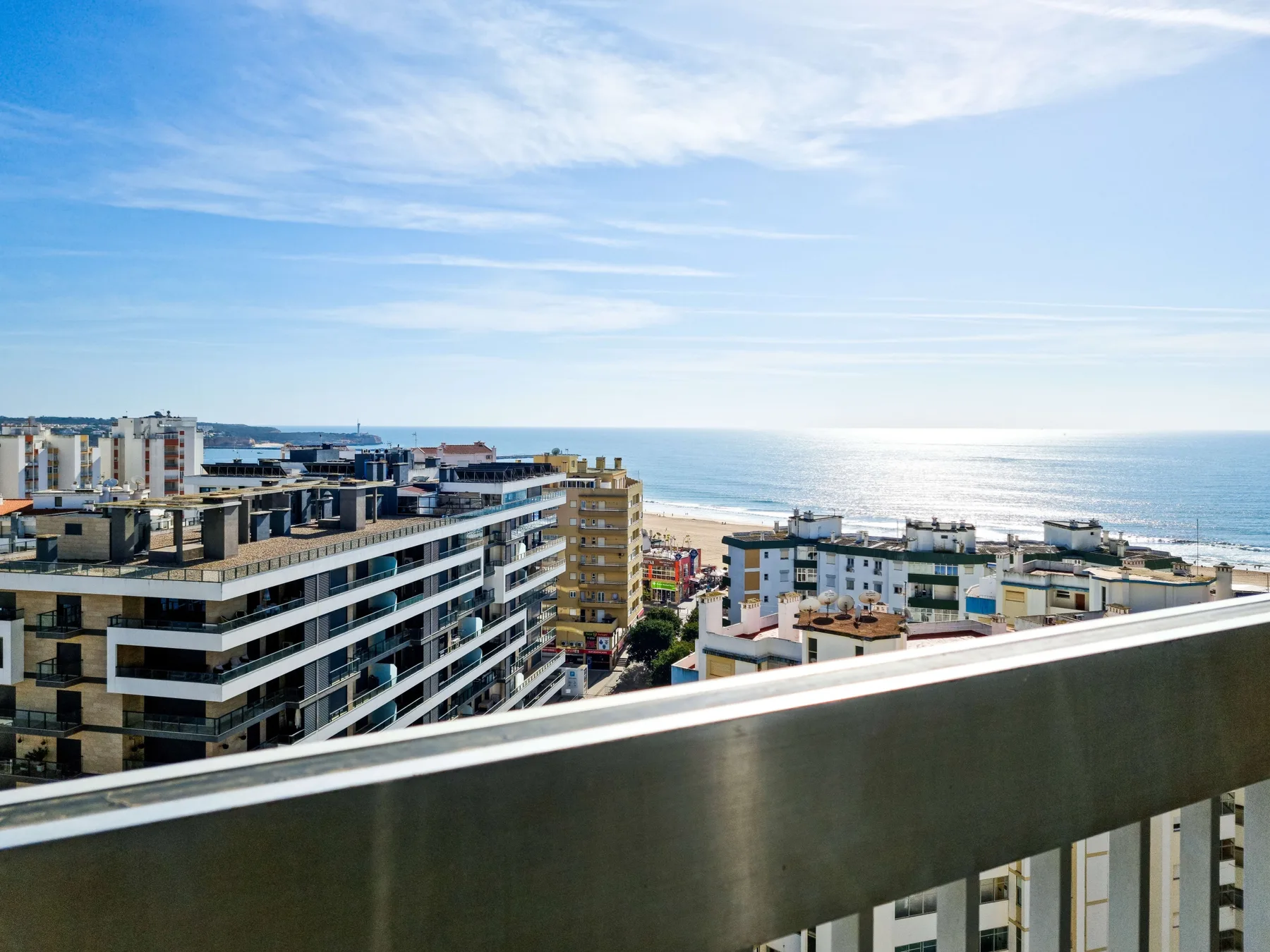 View of the coastline and ocean from a balcony, with buildings in the foreground.