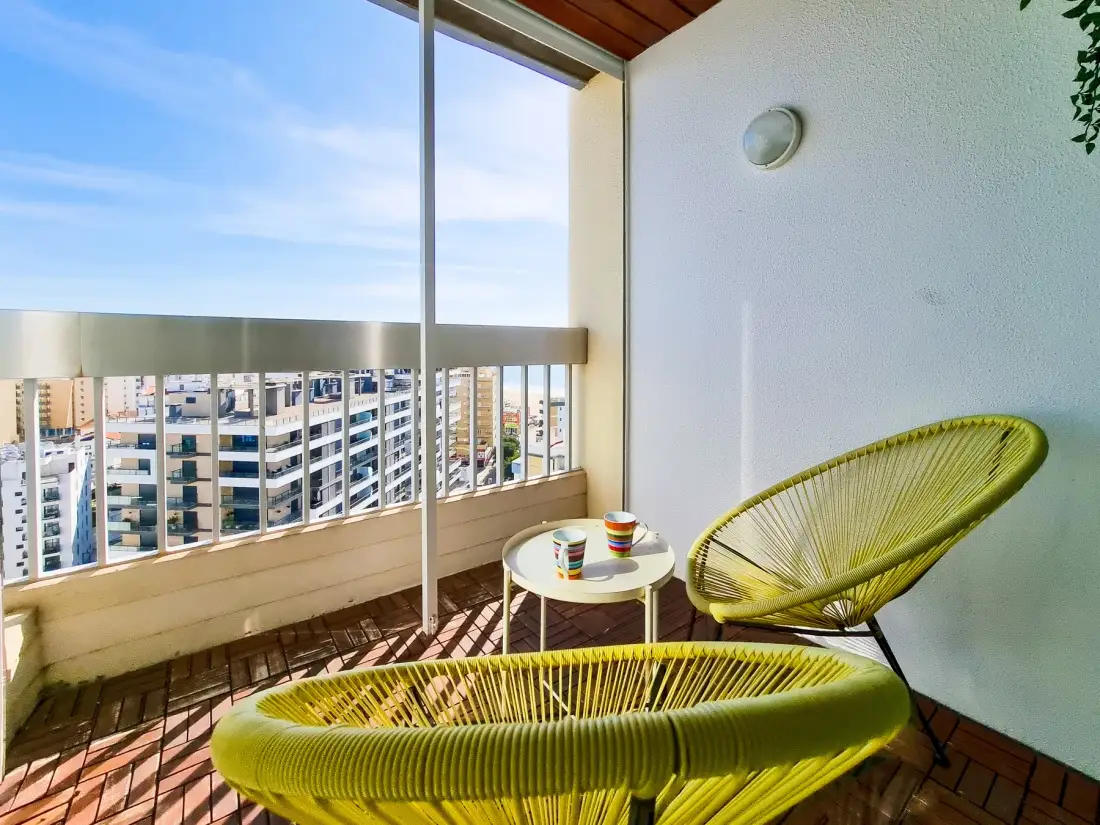 Un espacio de estar en el balcón con asientos tejidos y vistas a edificios cercanos.
