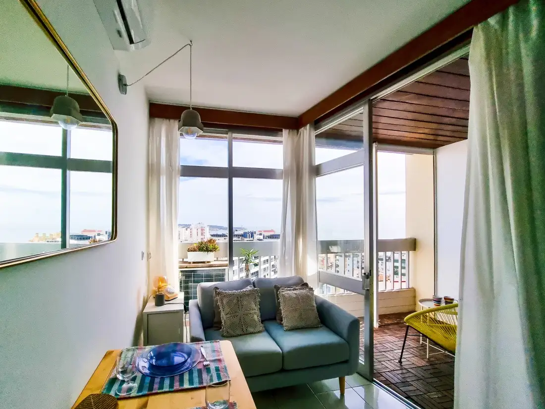 A living area with seating opens onto a balcony through large windows.