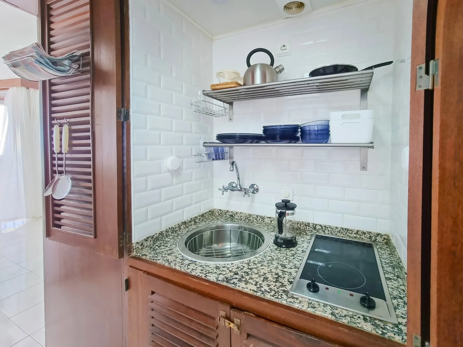 Una pequeña cocina con fregadero y placa de cocina bajo estantes.