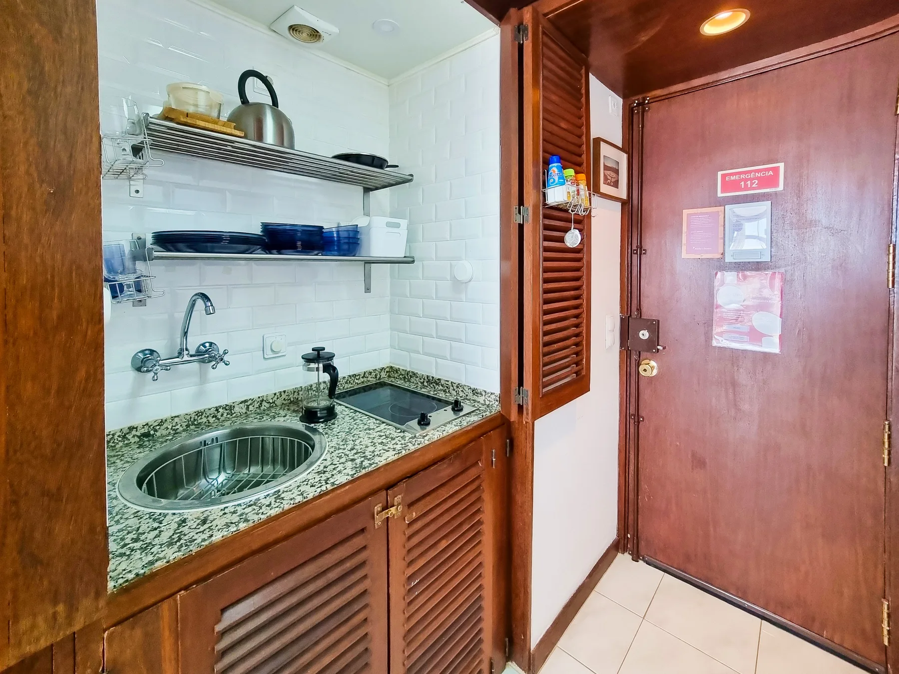 Una pequeña cocina con fregadero y placa de cocción junto a una puerta de entrada de madera.