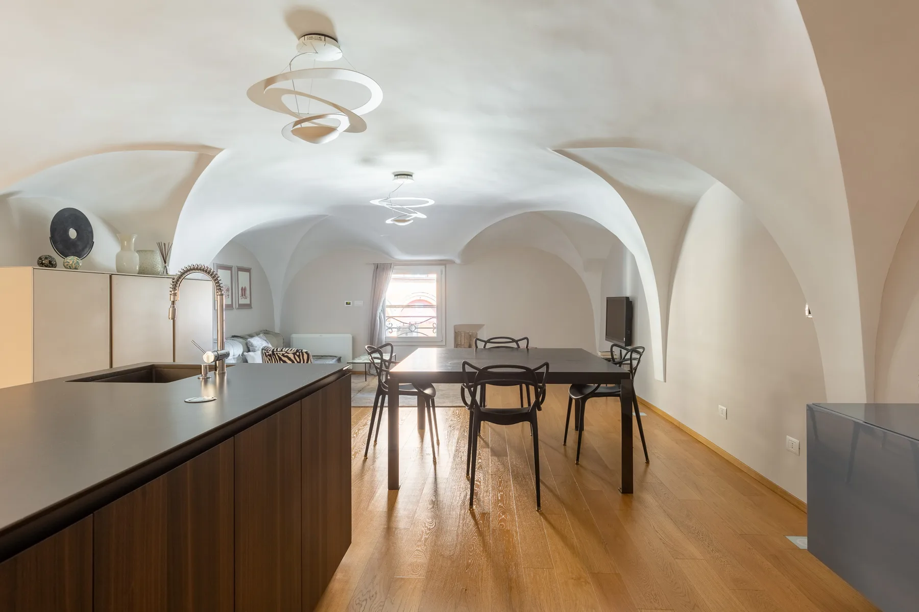 Un espacio abierto de comedor y cocina con una mesa larga bajo un techo abovedado.