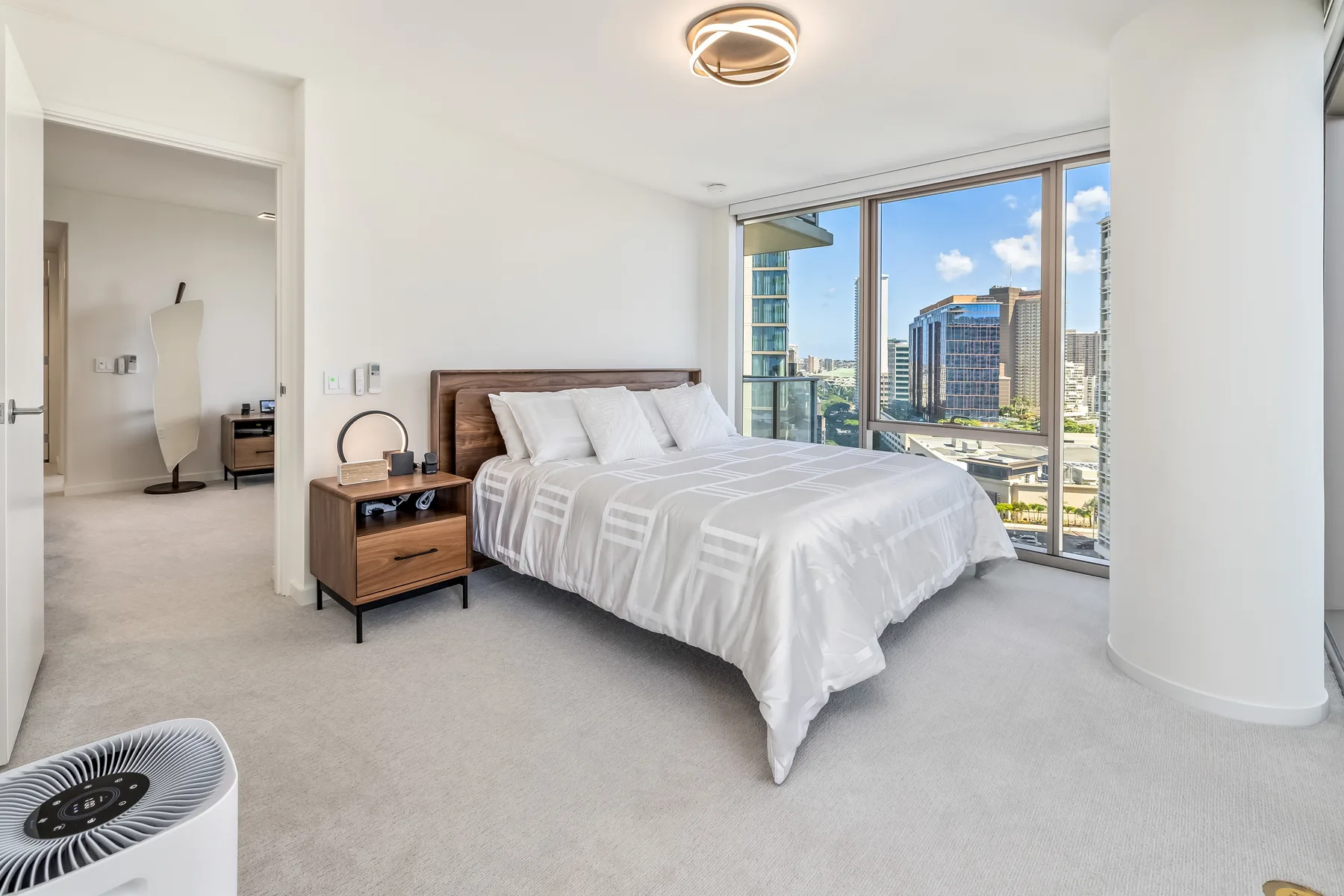 A bright bedroom with a neatly made bed beside large windows.
