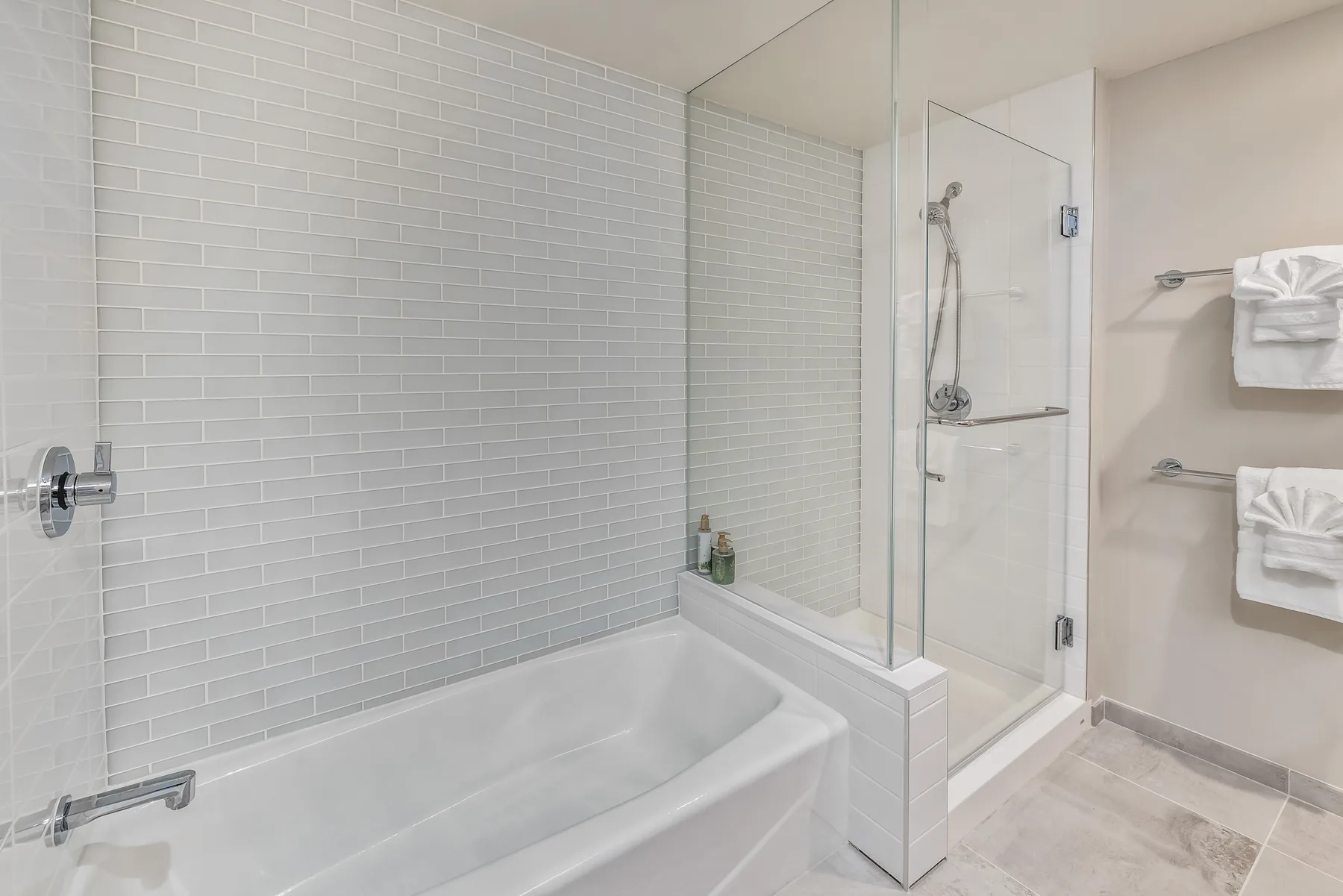 A bright bathroom with a bathtub, glass shower, and tiled walls.