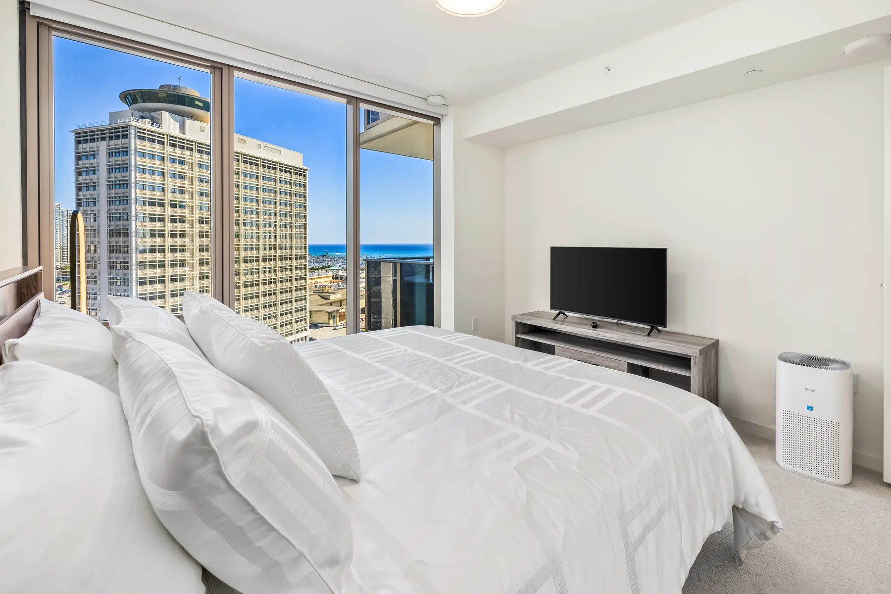 A bright bedroom with a large bed beside floor-to-ceiling windows.