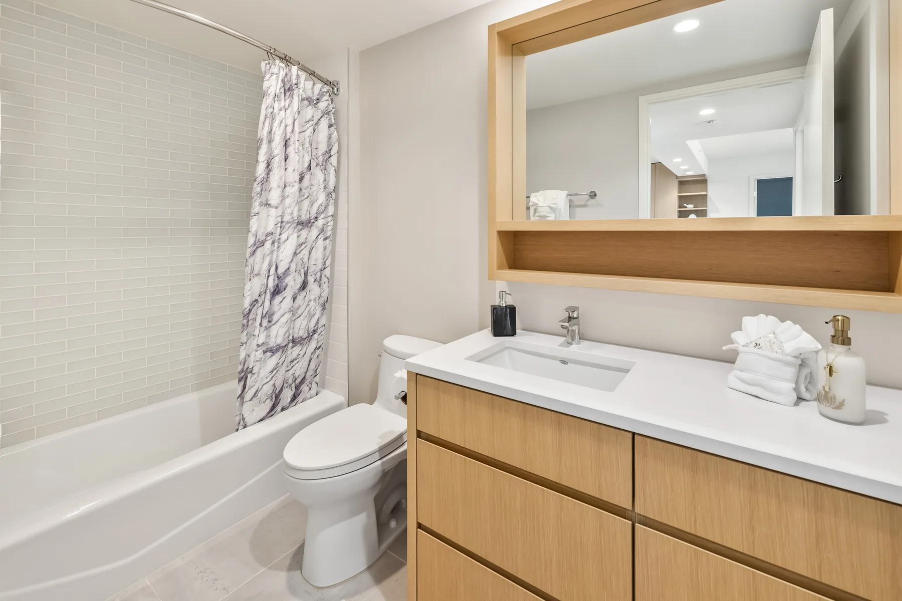 A bathroom with a bathtub, shower curtain, toilet, and wood vanity.