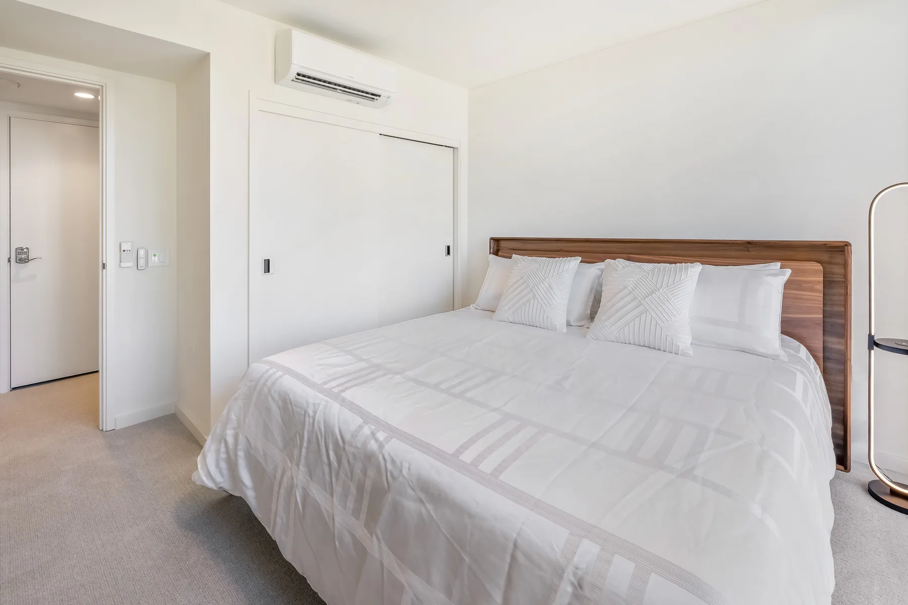 A bright bedroom with a neatly made bed and a wall-mounted air conditioner.