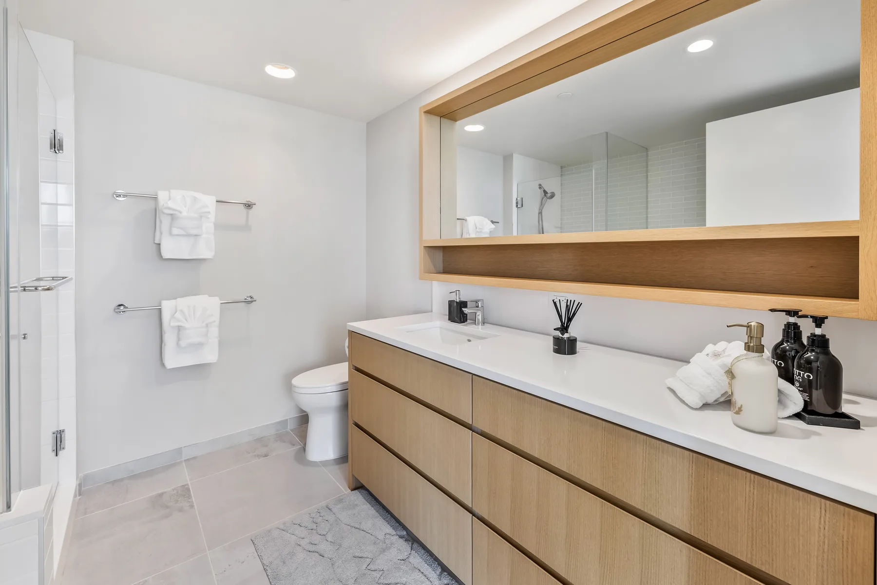 A bright bathroom with a long vanity, mirror, and shower.