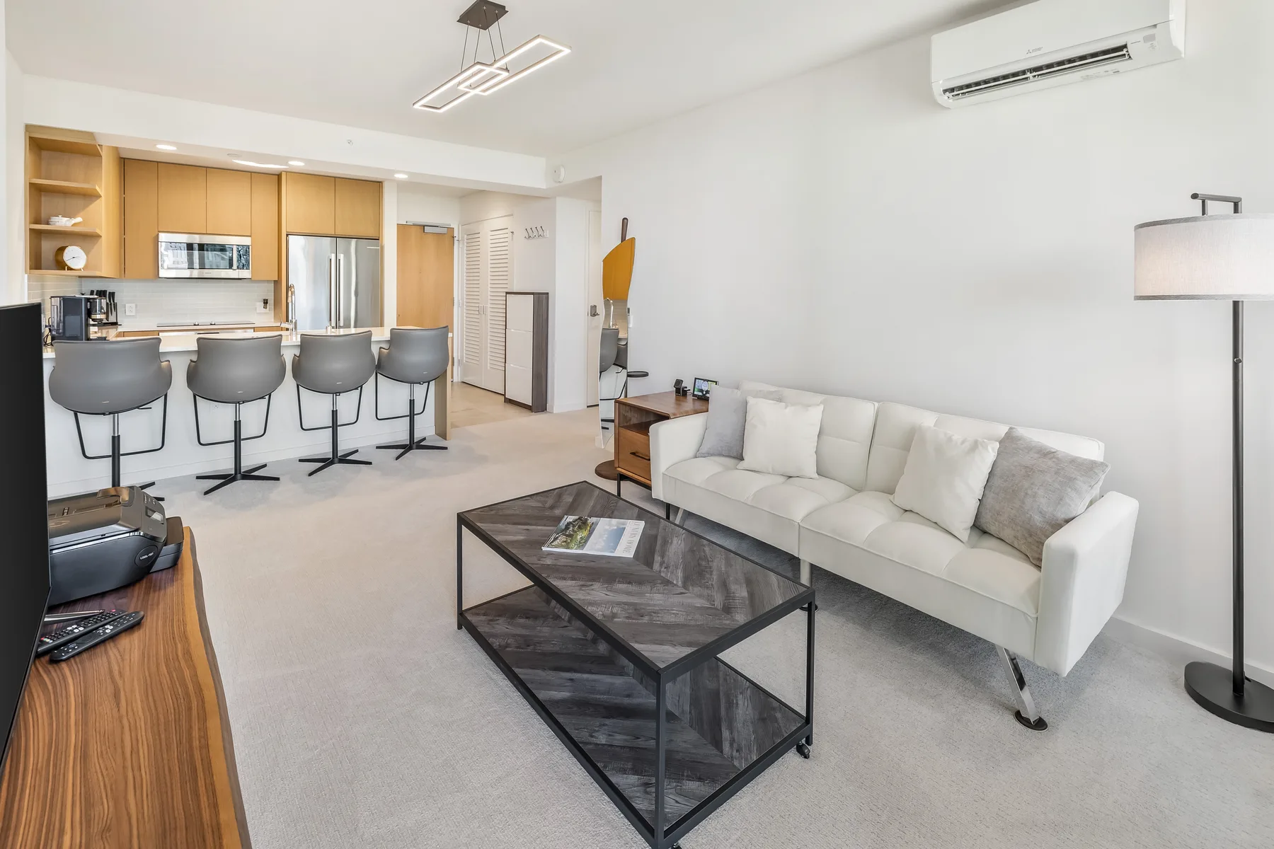 A bright open-plan living area with a white sofa and kitchen counter seating.