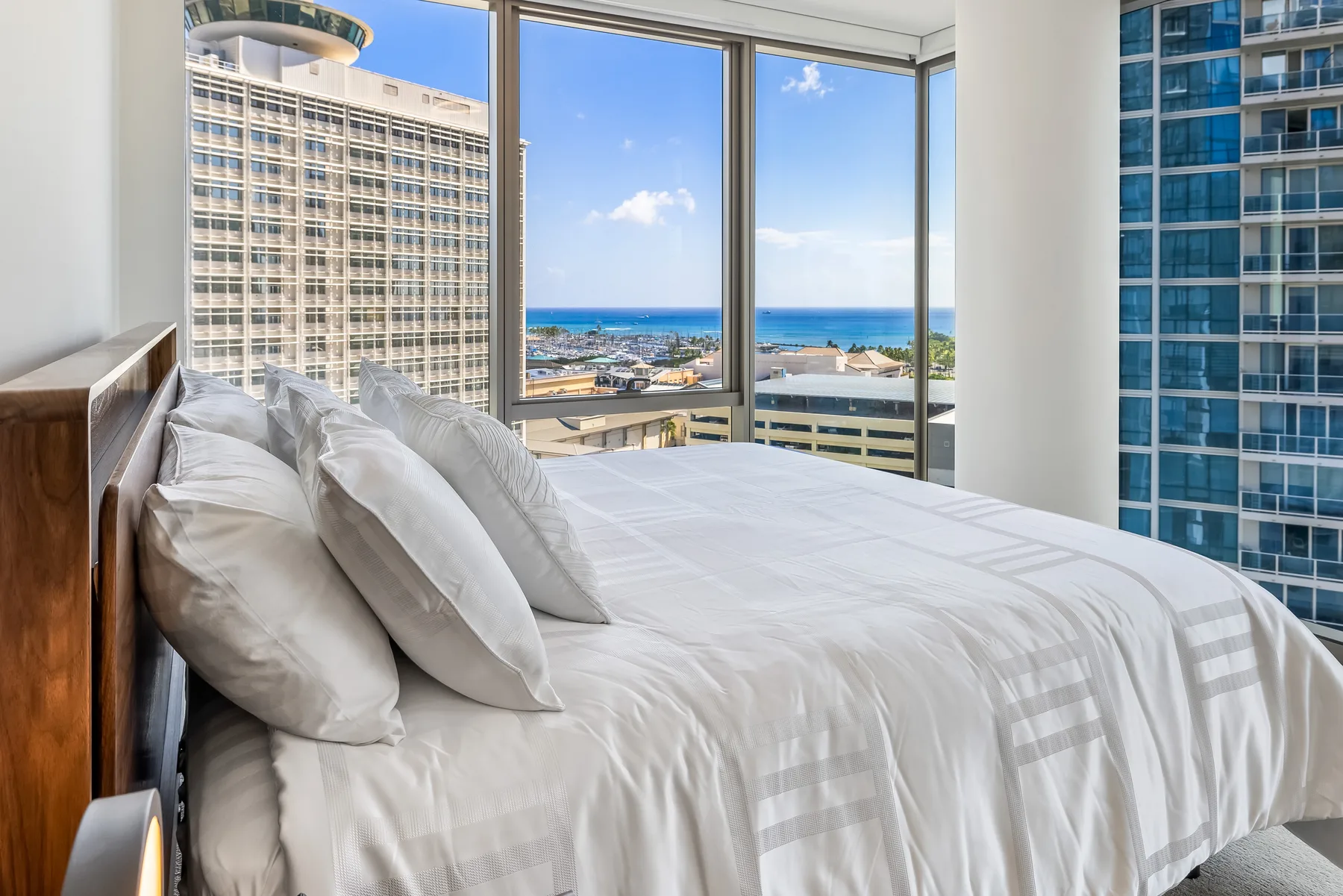 A bedroom with a neatly made bed beside large windows overlooking the ocean.