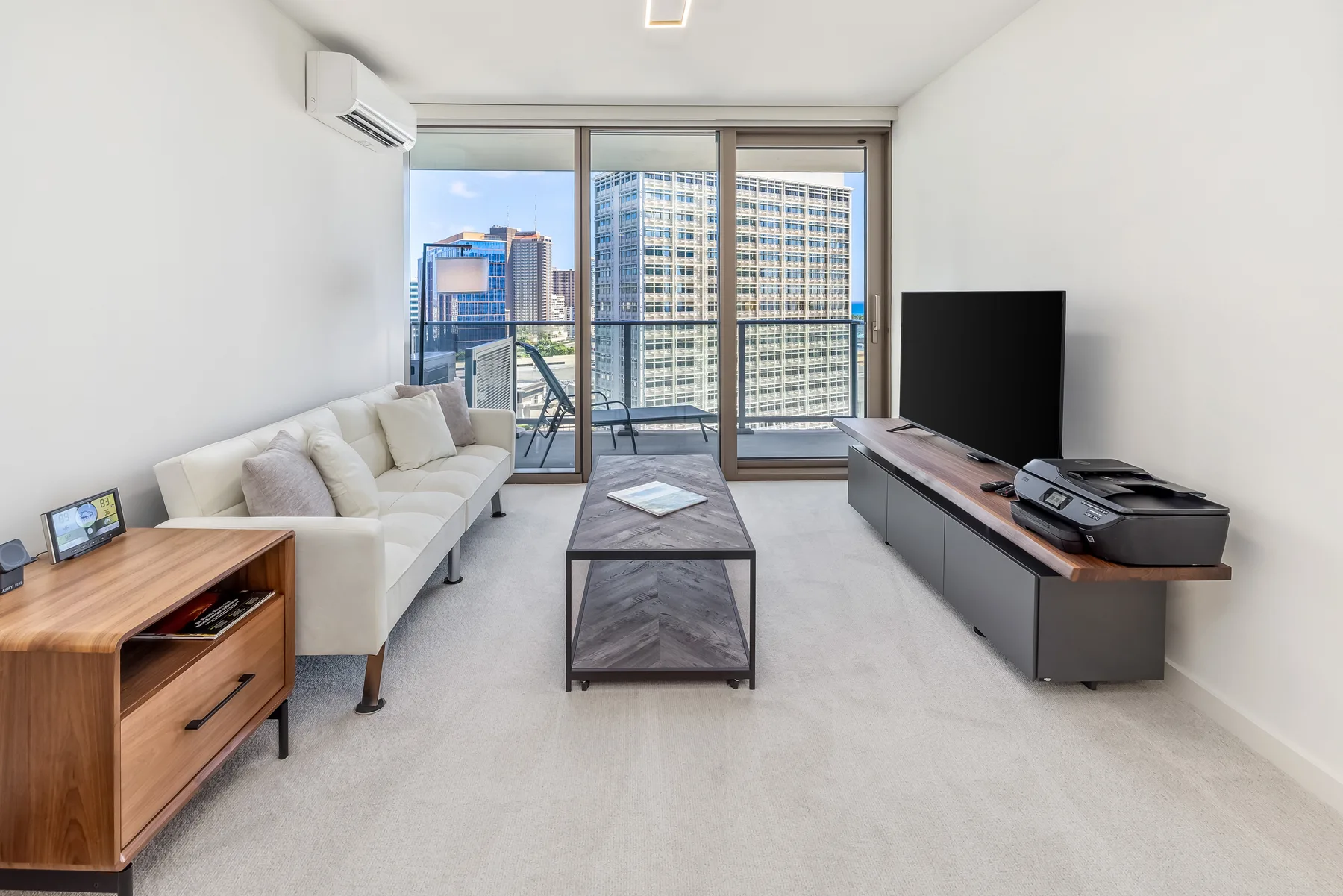 A bright living room with seating, a coffee table, and large windows overlooking nearby buildings.