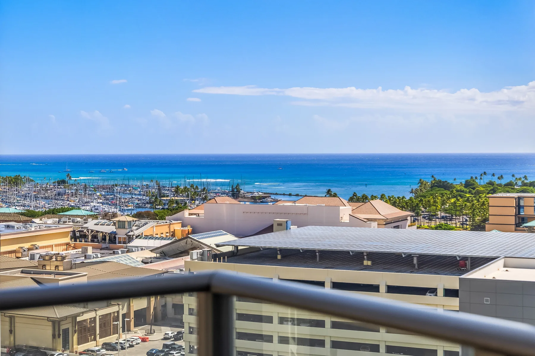 A balcony overlooks low-rise buildings and the ocean beneath a clear blue sky.