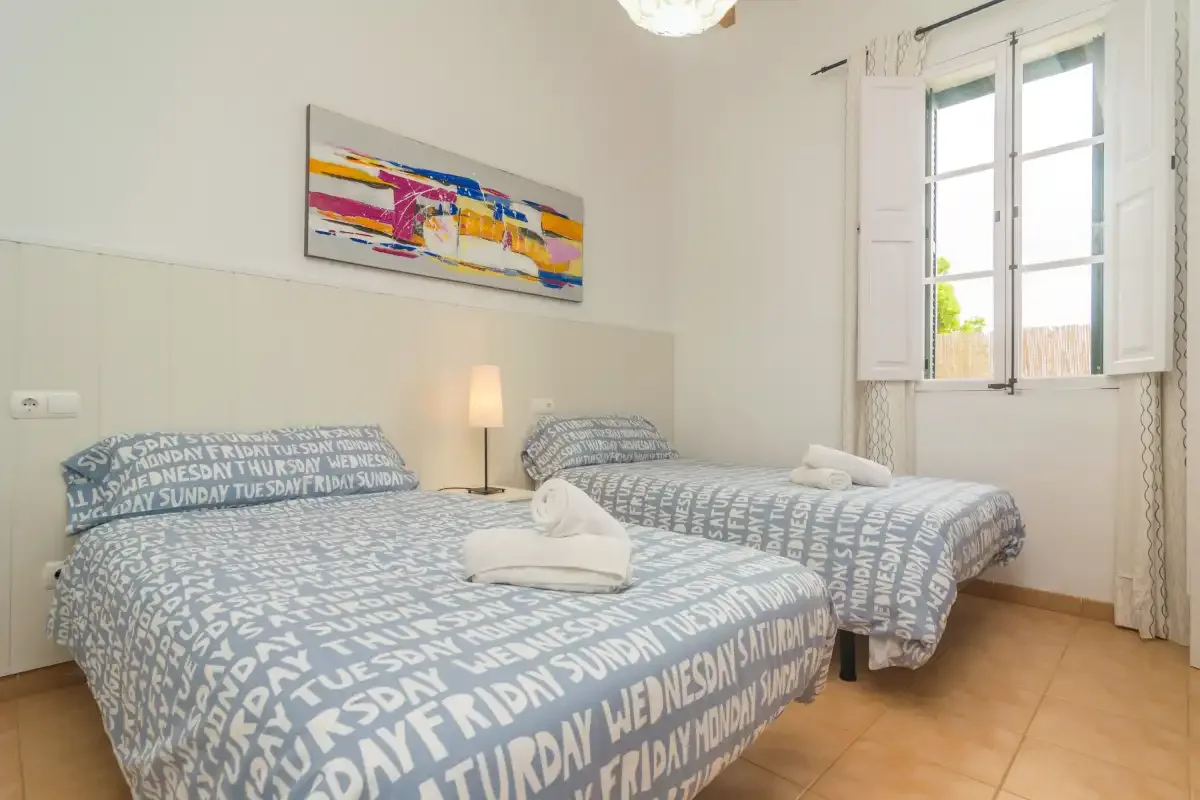 A bedroom with two beds, patterned bedding, and an open window.